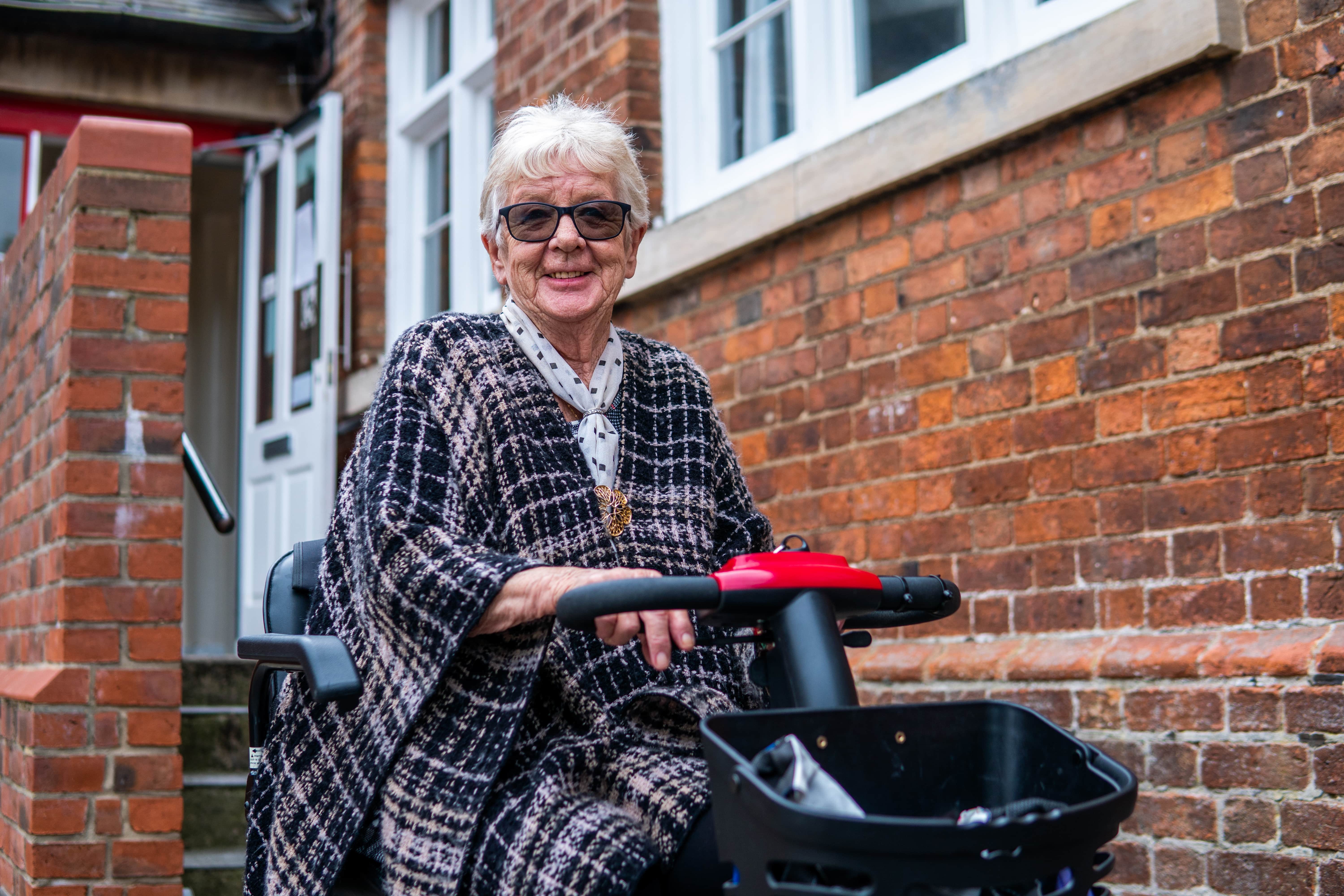 smiling woman using mobility scooter outside house