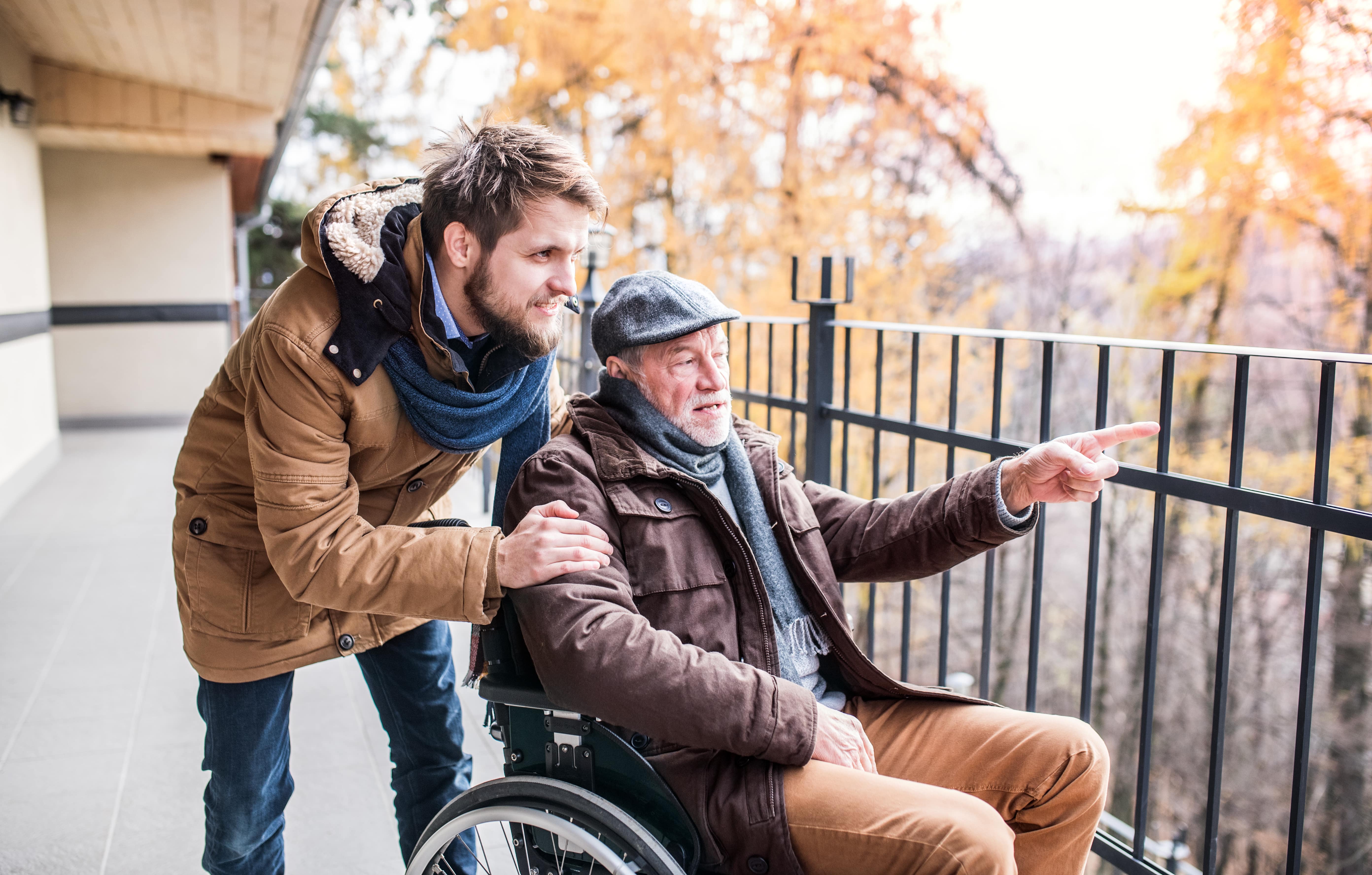 Young man leans close to older man in a wheelchair